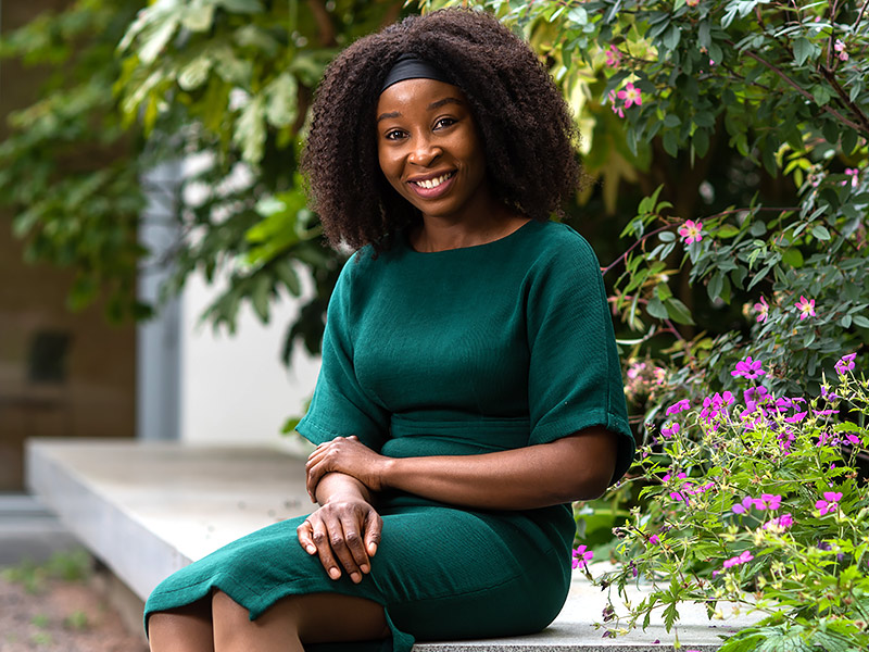 Crystal Chika Okwurionu sits outside at the Saïd Business School on a stone bench surrounded by plants