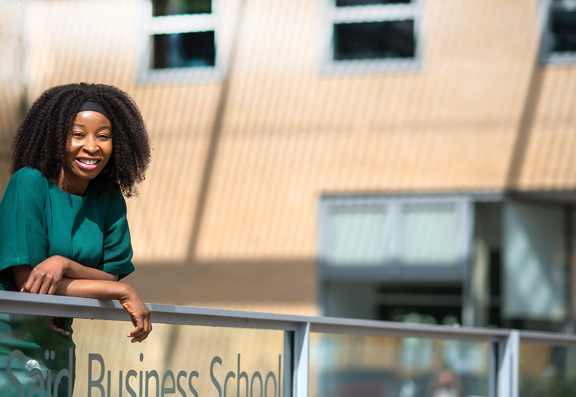 Crystal Chika Okwurionu leans forward against metal railings located just outside the entrance to the Saïd Business School