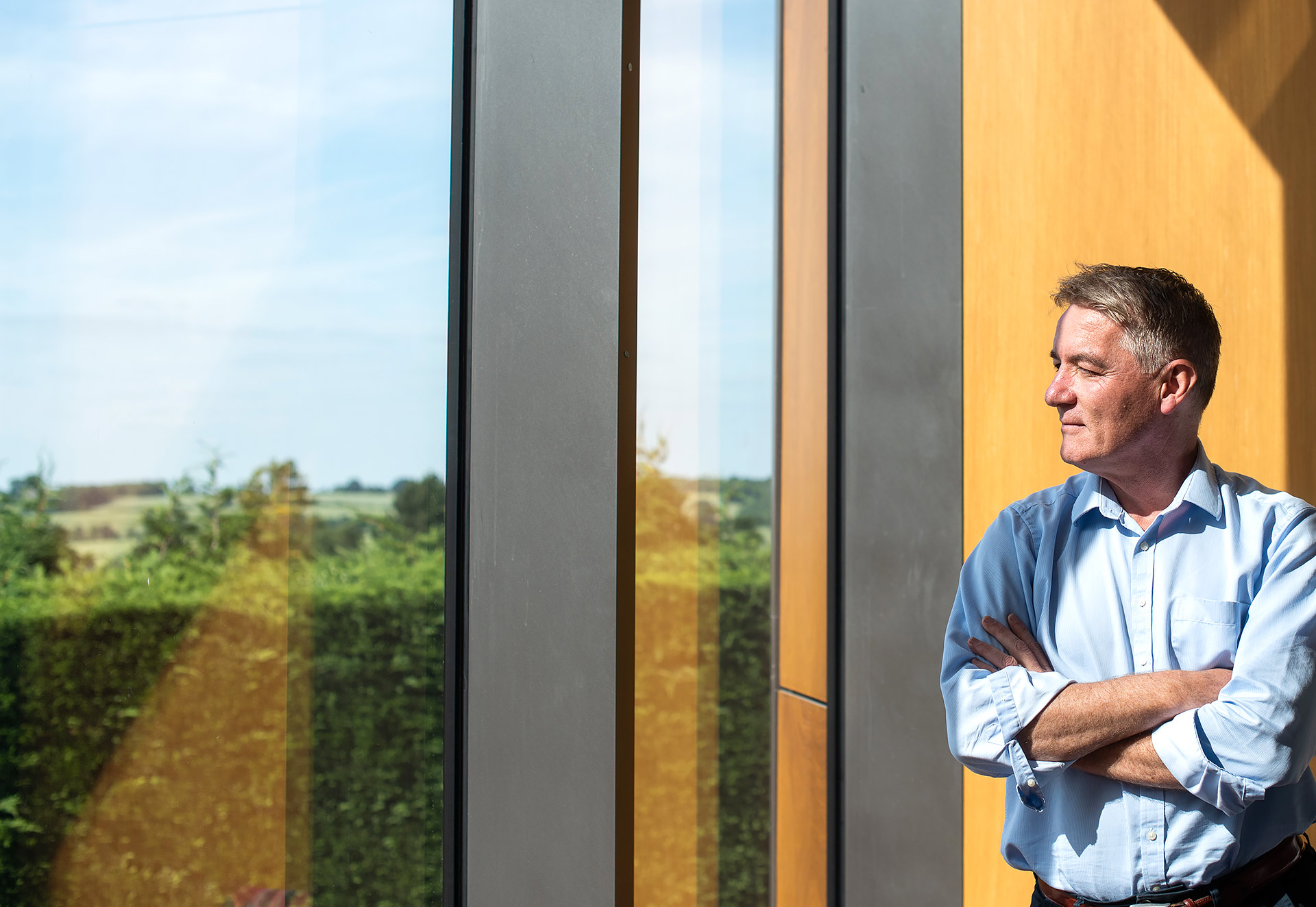 Peter Rothwell stands against warm wooden panelling looking out from the Wolfson Centre for the Prevention of Stroke and Dementia as the sun shines in through ceiling height windows