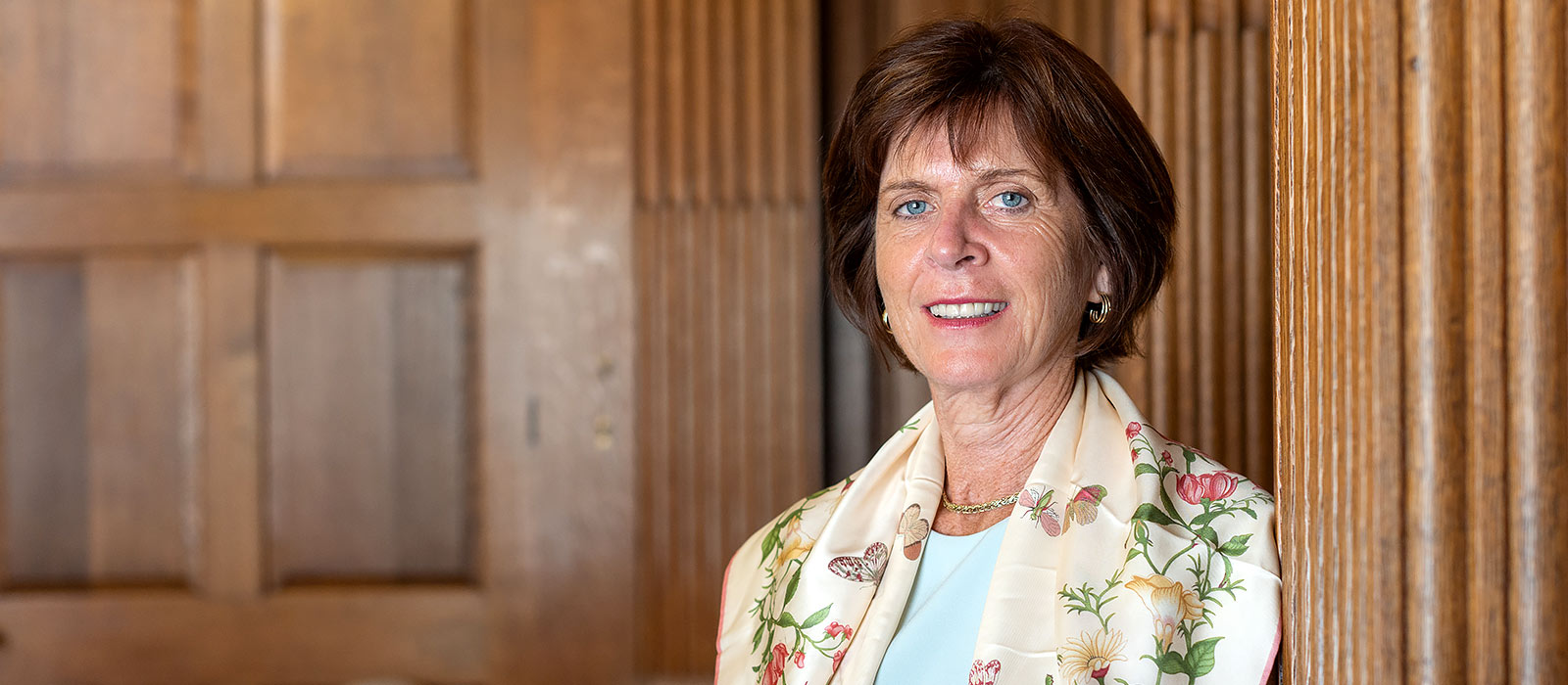 Professor Dame Louise Richardson leans against a wall in a wood-panelled room