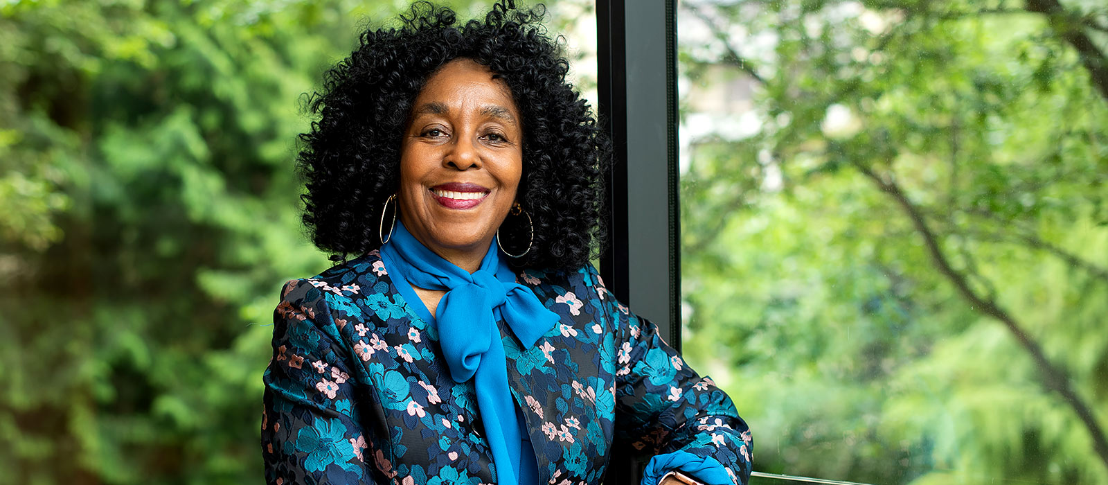 Professor Brenda Stevenson smiles as she stands at a window in St John’s College against a background of lush green gardens