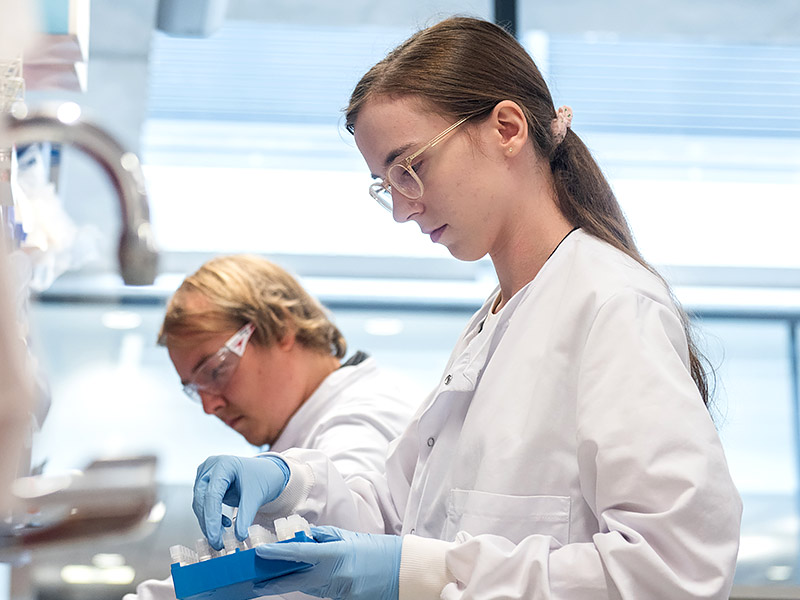 Postgraduate students working at the Jenner Institute in profile wearing lab coats and blue gloves