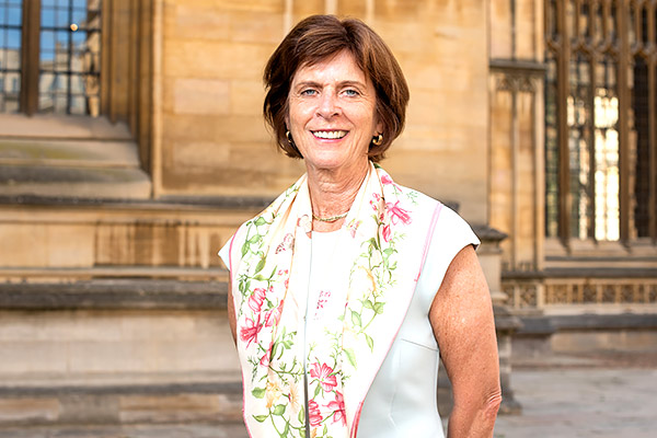 Professor Dame Louise Richardson stands in front of the ornate exterior of the Divinity School on a sunny day