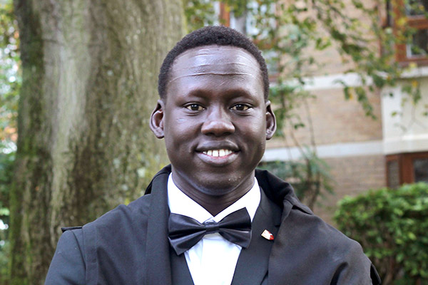 Lam Joar stands outside a college building wearing academic dress