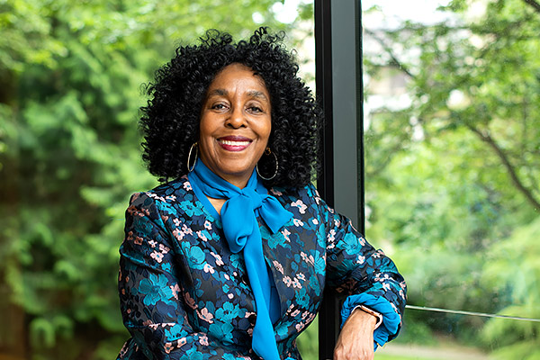 Professor Brenda Stevenson smiles as she stands at a window in St John’s College against a background of lush green gardens