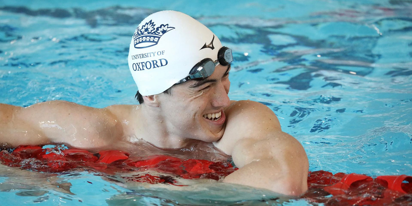 Swimmer in pool at the end of his race wearing a white Oxford University Swimming Club hat