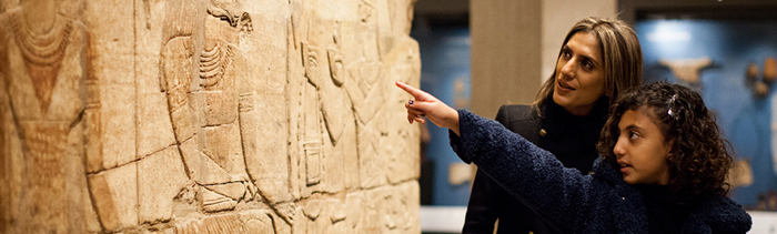 A young girl and her mother look at Egyptian reliefs in a museum gallery