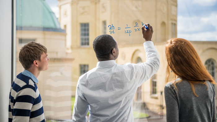 Students writing mathematical equations on window.