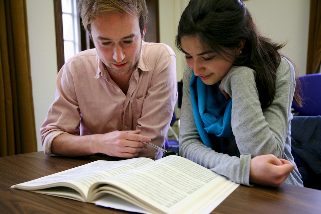 Photo of two students sat at a table together reading the same book