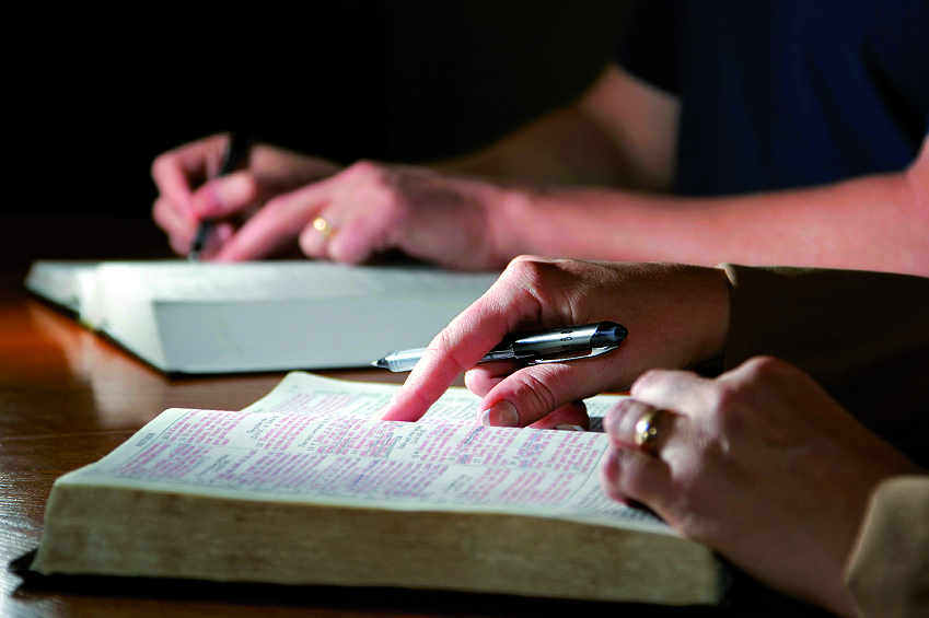 A photo which focusses on the hands of two students scanning books whilst sat at a table