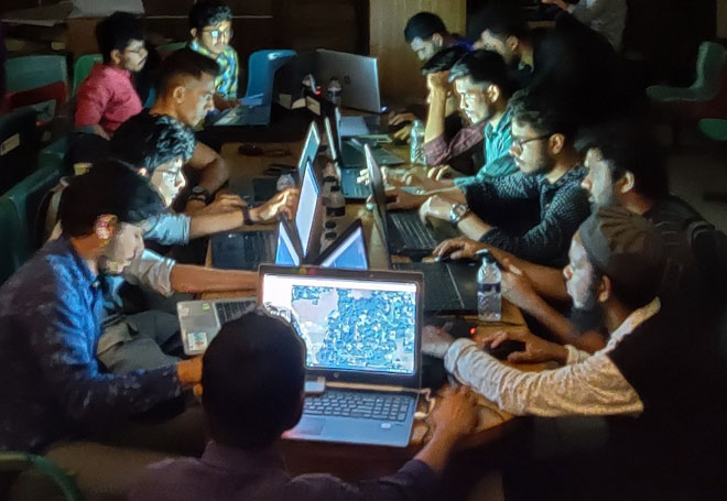 People sitting round a table at night, their faces lit up by the laptop screens in front of them