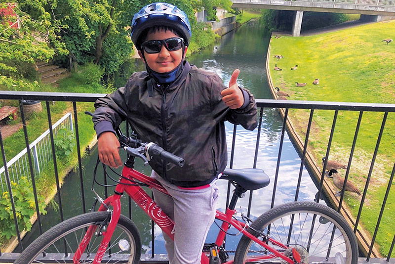 Nine-year-old Amol Neupane rides his bike over a bridge above a canal
