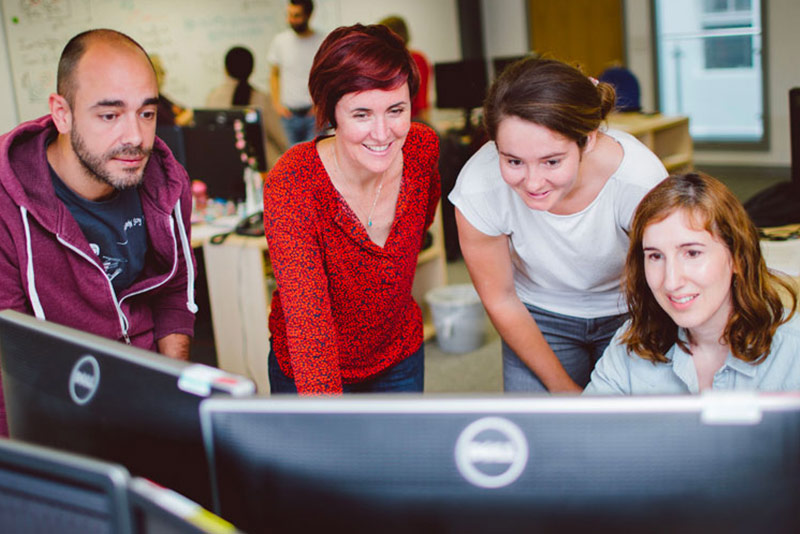 Four graduate computer science students gather around a computer monitor in a lab