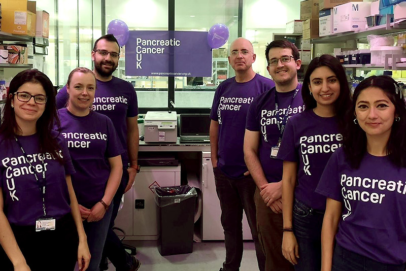 Eric O’Neill and his colleagues wear purple and white Pancreatic Cancer UK T-shirts as they stand together in a lab