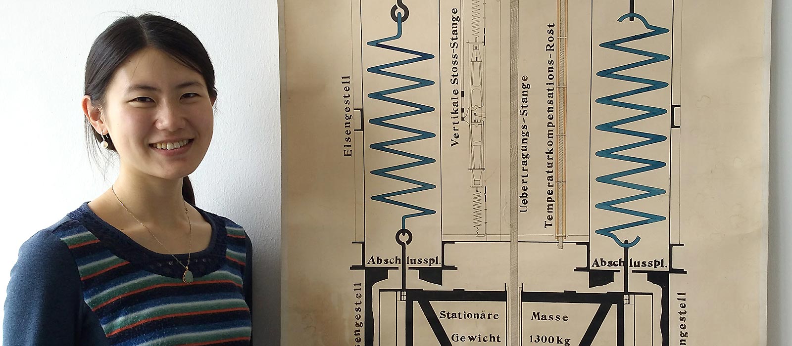 Qi at the University of Hamburg, standing in front of a design of one of the earliest seismometers. Photo by Celine Hadziioannou