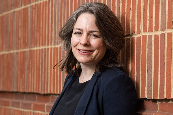 Professor Cathy Creswell leaning against a bright red brick wall in central Oxford