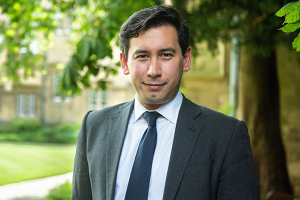 Dr Ben Caldecott stands in a leafy, shaded spot in one of Balliol College’s quads