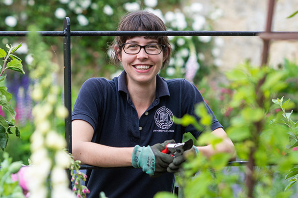 Apprentice Laura Quinlan smiles surrounded by bright, healthy-looking flowers and shrubs at the Oxford Botanic Garden