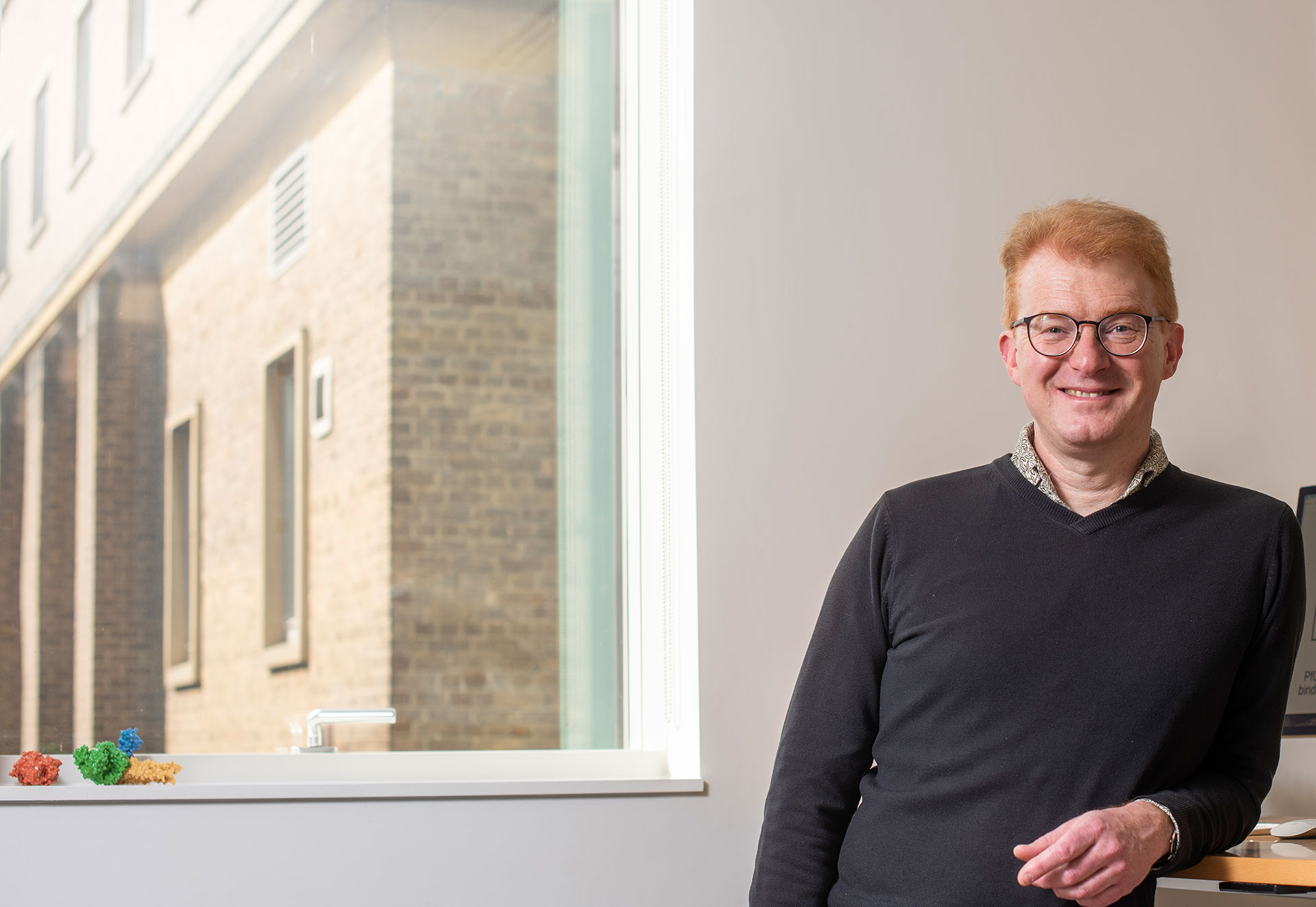 Peter Rothwell stands against warm wooden panelling looking out from the Wolfson Centre for the Prevention of Stroke and Dementia as the sun shines in through ceiling height windows