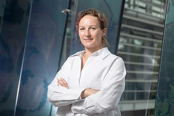 Professor Emma Slack stands with her arms folded against a dark green backdrop