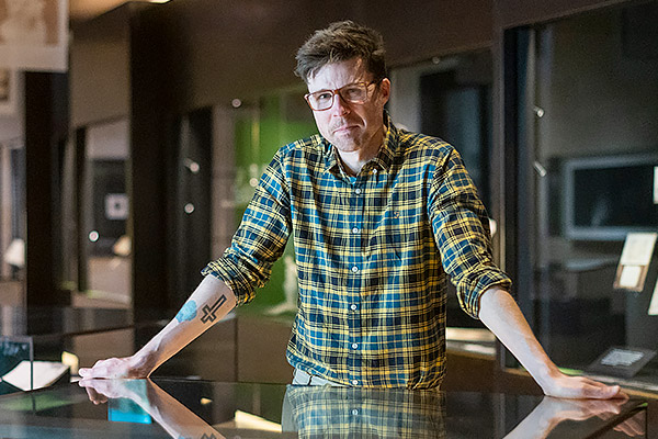 Dr Phillip Roberts leans against a glass exhibition case in the Bright Sparks photography exhibition