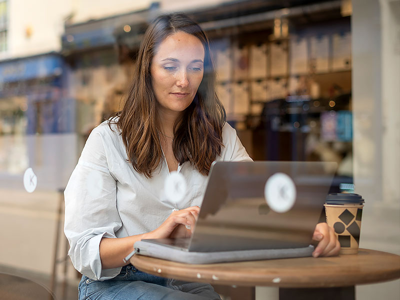 Lily Rodel works at her laptop in a café. A takeaway coffee cup sits on the table next to her. 