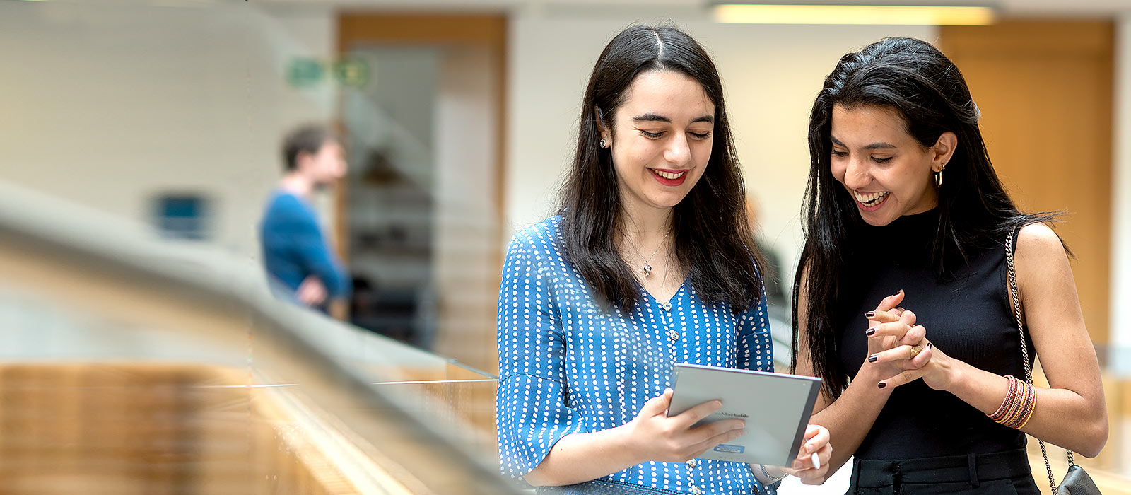 Two female graduate students stand chatting in the Andrew Wiles Building