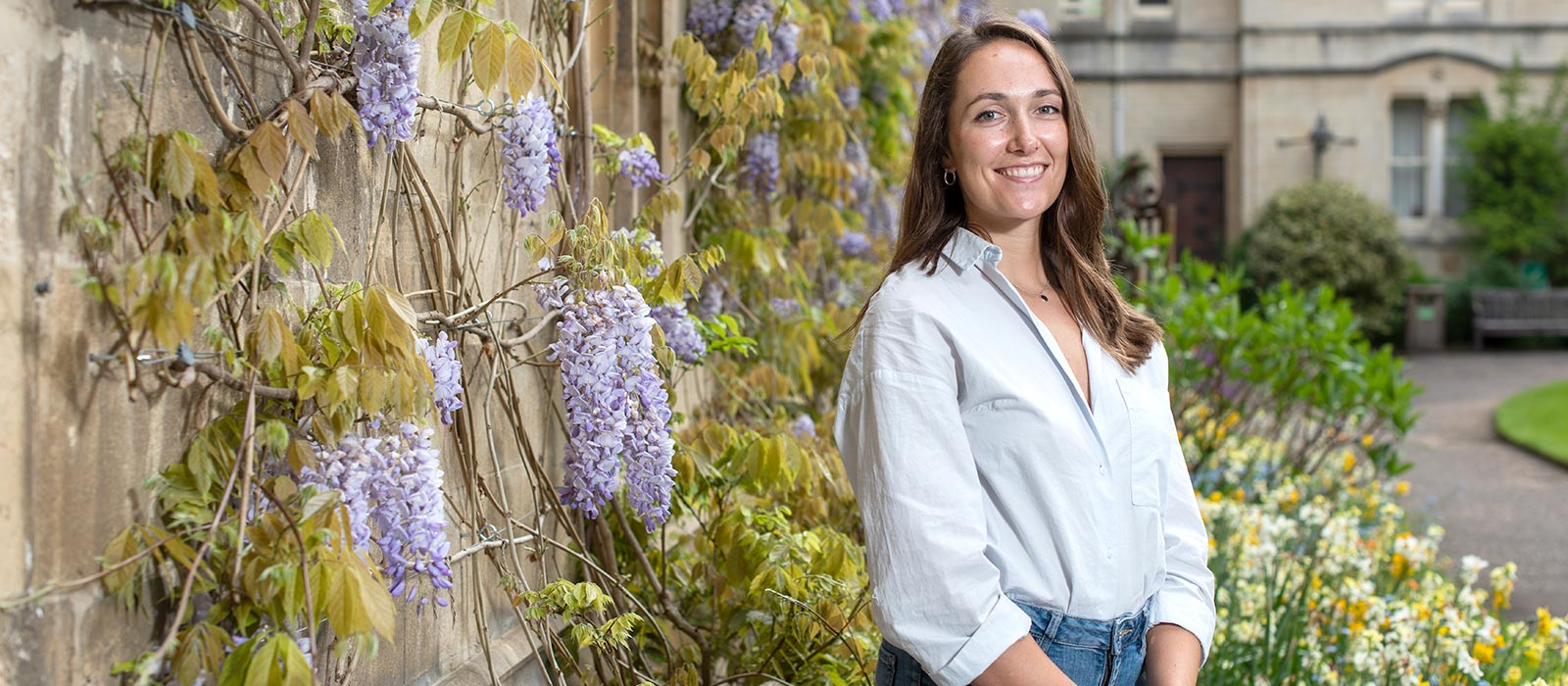 Lily Rodel stands in front of a wisteria-clad wall in the grounds of Balliol College