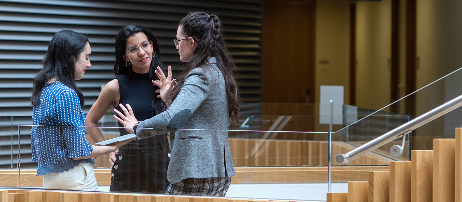 Three graduate students stand together chatting in the Andrew Wiles Building