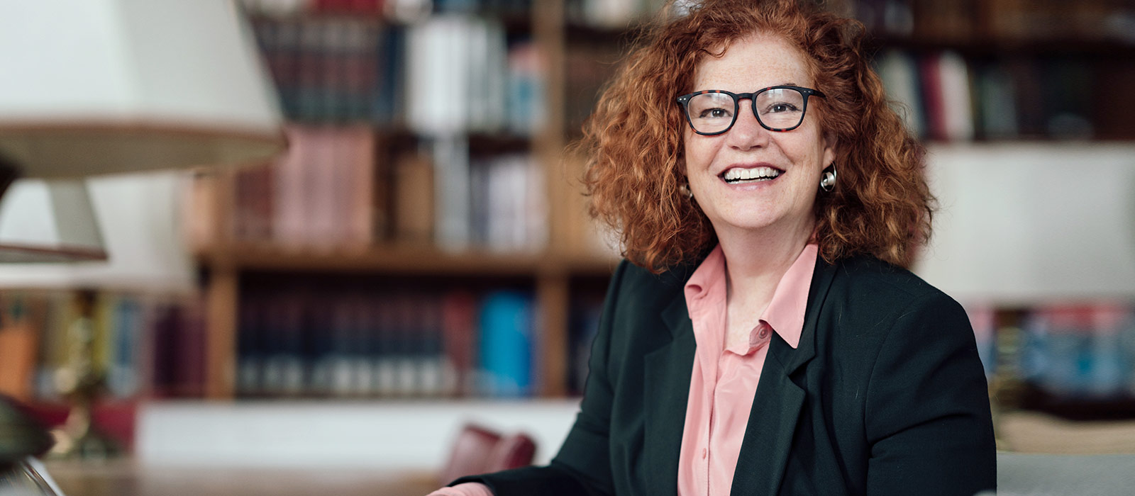 Professor Karen Leeder smiles in the Taylor Institution Library surrounded by books  