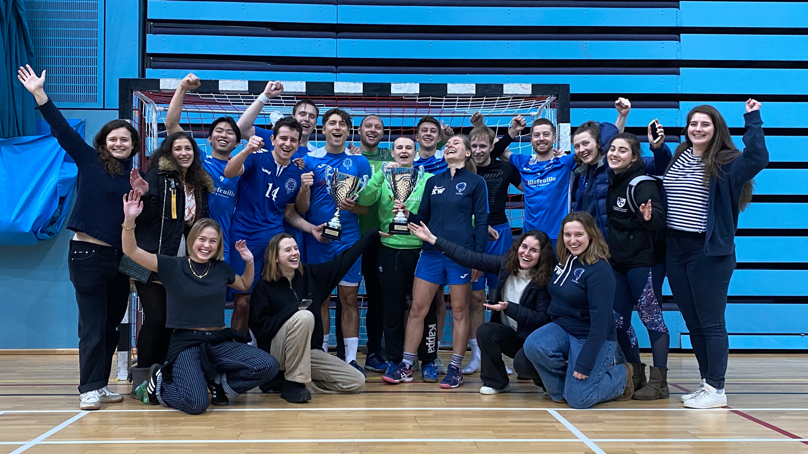 A team of handball players stand in front of a goal cheering