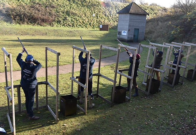 Photo of a group of shooters in seperate stalls all aiming to the sky ready to shoot