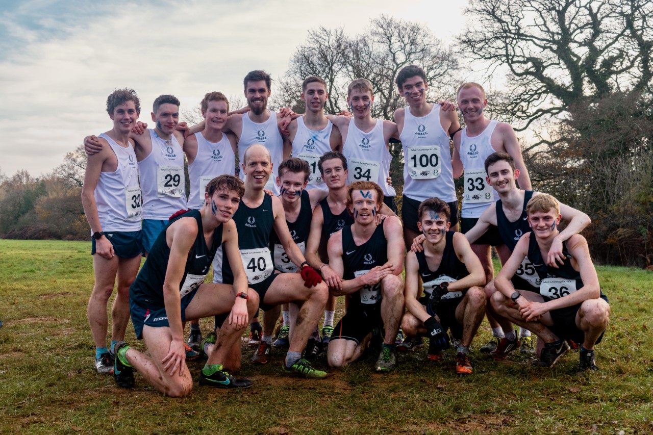 a group of 16 young men face the camera smiling, wearing OU Cross-Country kit and race numbers