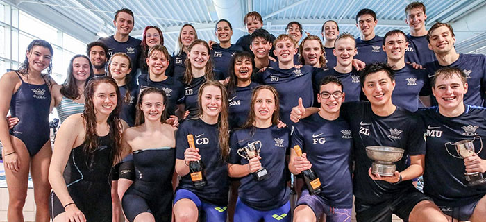 Oxford University Swimming Club team in blue kit, with the team captains holding competition trophies