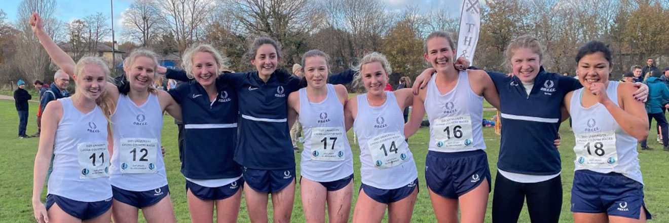 9 young women face the camera smiling, wearing OU Cross-Country kit and race numbers