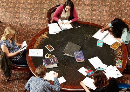 Photo of a group of students taking notes and studying at a large round table